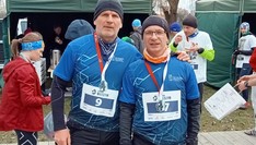 Biegacze w koszulkach Klubu Biegacza PRz na tle innych biegaczy i namiotów