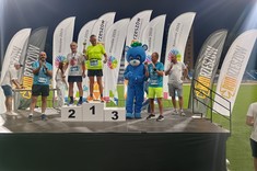 Zdjęcie przedstawia biegaczy stojących na podium z pucharami